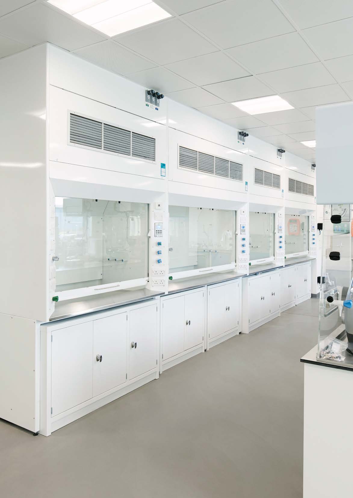 A clean, modern lab space featuring a row of fume hoods with transparent panels and white cabinetry below.